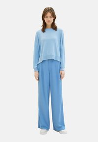 Lichtblauwe, cropped trui met lange mouwen, gecombineerd met losse, hoogstaande broek in bijpassend blauw. Witte sneakers. Zachte textuur.