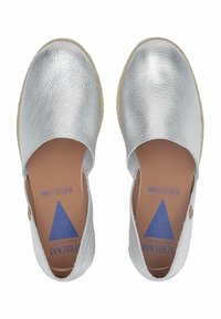 Espadrilles metálicas de plata con una textura suave, diseño sin cordones y una plantilla de color tostado que presenta un logo de triángulo azul en el lado interno.