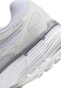 Gros plan sur la semelle et la tige blanche et grise d'une chaussure de sport avec tissu en maille, superpositions cousues et marquage "P-6000" sur le côté.
