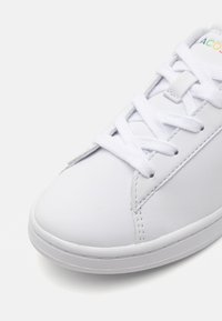 Sneaker bianco con tomaia in sintetico liscio, design con lacci, punta arrotondata e suola piatta in gomma. Presenta dettagli di cucitura discreti.