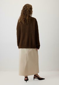 Oversized brown knit sweater with textured pattern, paired with a beige ankle-length skirt. Black slingback heels complete the outfit.