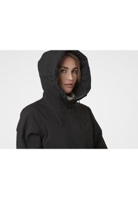 Černá vycpaná bunda s vysokým límcem a velkou kapucí. Obsahuje elastické šňůrky, zipové zapínání a hladkou vnější strukturu.