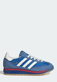 Modrá semišová a textilní teniska s bílými pruhy, gumovou podrážkou a červenými detaily. Má texturovaný podpatek a zavazování na tkaničky.