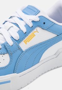 Sapatilha de couro azul com detalhes brancos, atacadores brancos e um logotipo dourado. Superior texturizado com um design elegante e colarinho acolchoado.