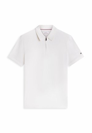 Polo blanco de manga corta con cuello y cremallera frontal, con el logo de Tommy Hilfiger en la manga izquierda.