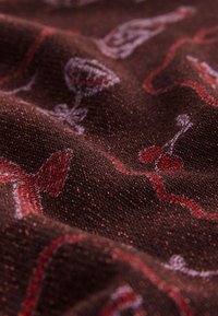 Tissu brun texturé avec une finition scintillante, présentant des motifs ludiques de verres à vin, cerises et lignes ondulées en rouge et violet.