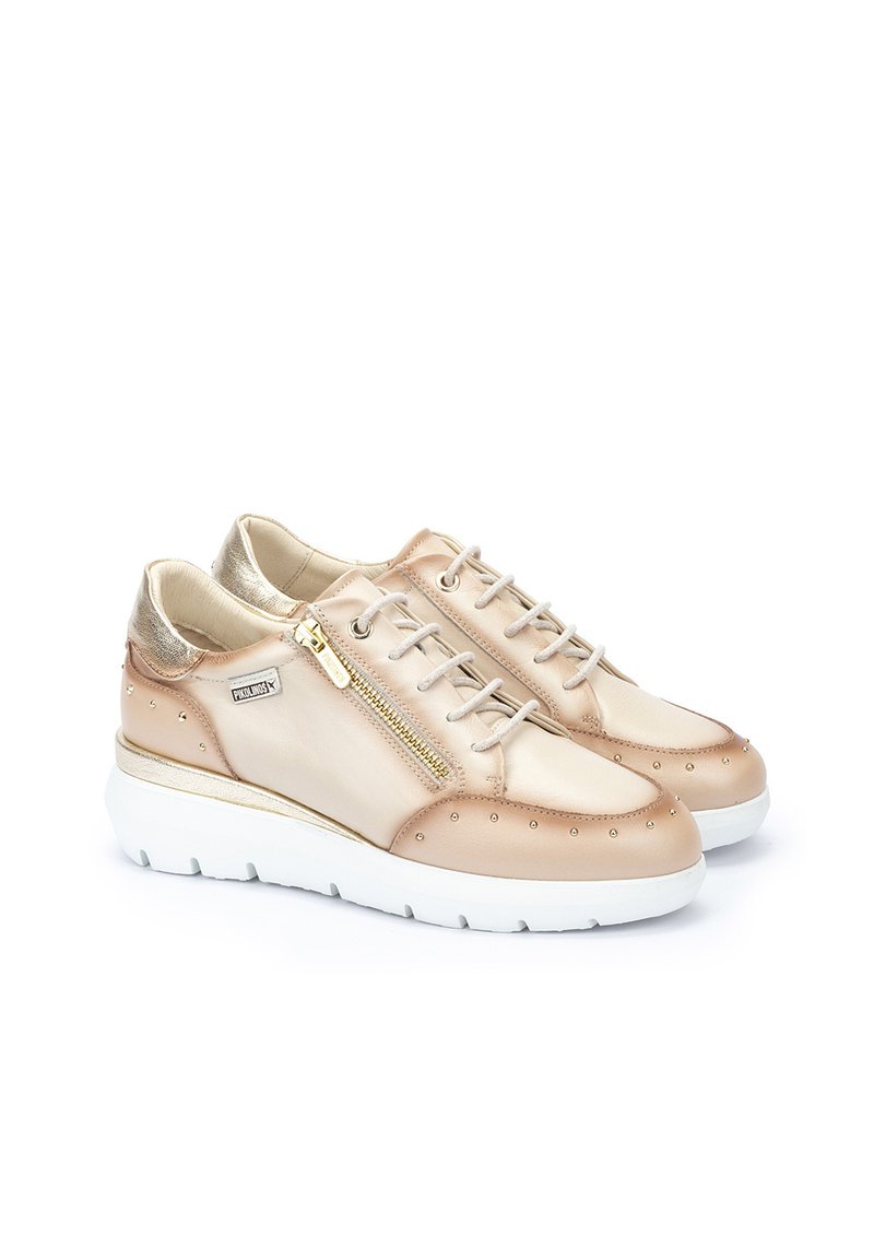 Zapatillas de cuero beige con acentos metálicos, tachuelas decorativas y un zipper lateral. Suela acolchada con una base blanca y un acabado texturizado.