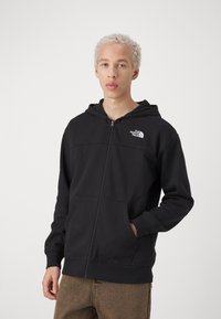 Czarna bluza z kapturem na zamek wykonana z gładkiego materiału, z przednią kieszenią, z małym białym logo na lewej piersi i sznurkiem ściągającym w kapturze.