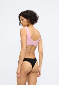 Bralette rose à dos nu et string noir avec des détails festonnés. Texture lisse avec des bretelles larges et un design minimaliste.