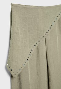 Tissu en lin vert olive clair avec un bord drapé orné d'une rangée diagonale de petites rivets métalliques ronds réfléchissants.