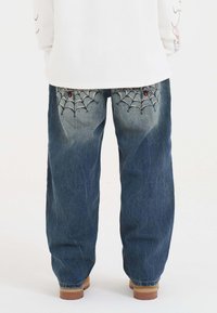 Denimjeans i mörkblått med lös passform, med spindelnätsbroderi på bakfickorna och en texturerad yta.