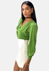 Blusa di raso verde con frontale drappeggiato e maniche a sbuffo, abbinata a una mini gonna bianca attillata con una zip laterale.