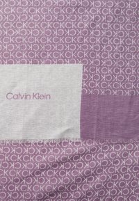 Il foulard Calvin Klein presenta un tessuto a fantasia viola con ripetuti loghi "CK", arricchito da una sezione bianca uniforme che mostra il nome del marchio.
