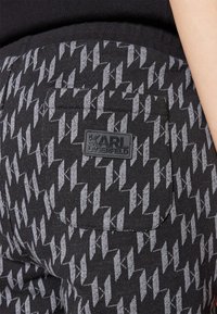 Čierne bežecké nohavice s šedým zigzag vzorom, zadnou vreckom a čiernou gumovou nášivkou s nápisom "KARL LAGERFELD".