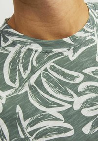 Groene t-shirt met een ontwerp van witte bladeren. De stof ziet er zacht uit met een ronde hals en zichtbare stiksels.