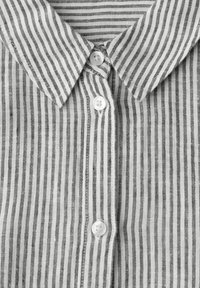 Chemise à col avec fines rayures verticales noires et blanches et boutons blancs sur le devant.