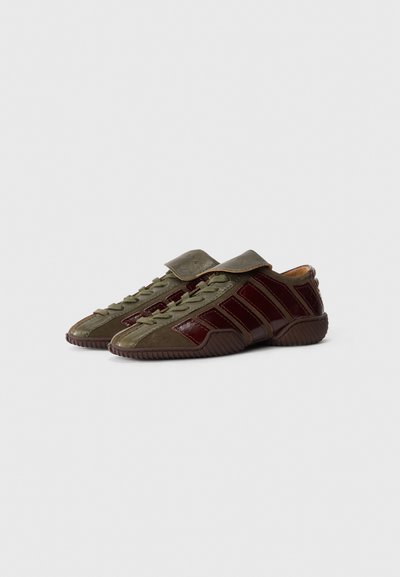 Green and burgundy shoes with a textured surface; features a strap, lace-up design, and ridged sole; glossy accents in burgundy.