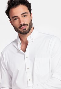 Witte overhem Longs met een borstzak, klassieke kraag en metalen knopen. De zachte textuur en getailleerde pasvorm verbeteren het algehele ontwerp.