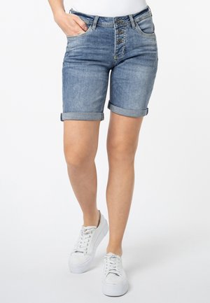 Hellblaue Jeansshorts mit umgeschlagenen Säumen, Fünf-Taschen-Design und Knopfverschluss. Kombiniert mit weißen Sneakers.