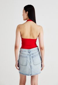 Rode haltertop met een aansluitend ontwerp, gecombineerd met een lichtblauwe denim minirok met achterzakken en een lichtgerafeld zoom.