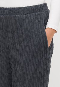 Pantalons texturés gris foncé avec un motif ondulé, taille élastique et poches latérales. Le tissu semble doux et légèrement extensible.