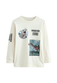 Långärmad krämfärgad T-shirt med dinosaurie-grafik i olika färger. Texten lyder "Dinosauriernas Värld" och "Förhistoriska Legender."