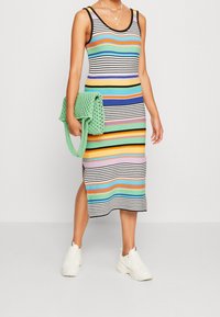Robe midi rayée multicolore avec une silhouette ajustée. Confectionnée en tissu côtelé. Assortie à un sac à main vert texturé et des baskets blanches.