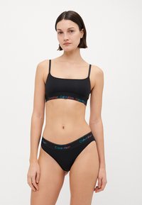 Svart bralette og truse-sett med tynne stropper, med et flerfarget logobånd. Mykt, elastisk materiale med et enkelt design.