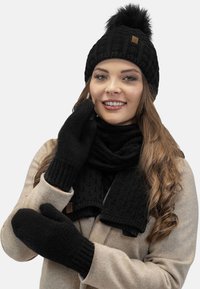 Sort strikket hue med en pom-pom, matchende sort scarf og vanter. Ribbet tekstur, med et brunt lædermærke på huen.