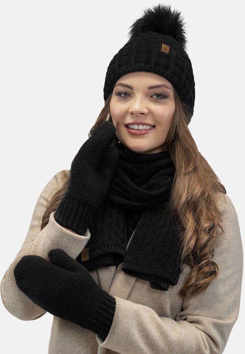 Sort strikket hue med en pom-pom, matchende sort scarf og vanter. Ribbet tekstur, med et brunt lædermærke på huen.