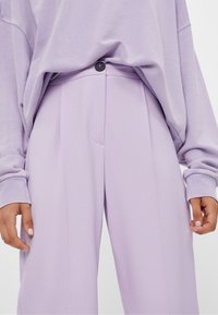 Lila losse broek met een enkele zwarte knoop, voorzien van plooien en een soepele textuur, gecombineerd met een bijpassende oversized lila top.