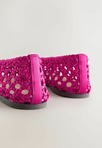 Paire de chaussures plates tissées magenta avec texture tressée et semelles noires, vues de dos sur fond blanc.