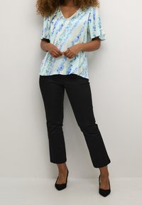 Top azzurro a vestibilità comoda con motivi astratti nelle tonalità di blu e verde, abbinato a pantaloni neri aderenti e décolleté neri a punta.