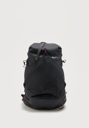 Mochila grande negra para senderismo con bolsillo frontal de malla, correas ajustables y acentos rojos, de pie sobre un fondo blanco.