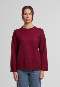 Burgundy színű kötött pulóver, kerek nyakkivágással, lezser vállakkal, bordás mandzsettákkal és alsó szegéllyel, puha tapintású anyagból készült.