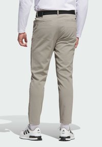 Beżowe spodnie o wąskim kroju, z czarnym paskiem, dwoma tylnymi kieszeniami oraz podwiniętymi nogawkami. Noszone z białymi butami i czarnymi akcentami.