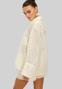 Witte getextureerde jas met een kraag, lange mouwen en franjes. Heeft een losse pasvorm en een zachte, doorzichtige stof.
