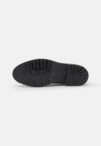 Suela de zapato de goma negra con patrón estriado para tracción, con forma redondeada y textura suave. Área de puntera reforzada para mayor durabilidad.
