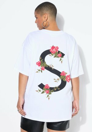 Weißes, übergroßes T-Shirt mit einem großen schwarzen "S" auf dem Rücken, verziert mit roten Rosen und grünen Blättern, aus Baumwollmaterial.