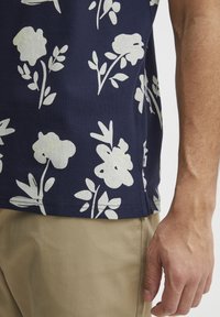Marineblå kortermet skjorte med et hvitt blomsterdesign, laget av teksturert stoff. Kombinert med khaki bukser, som viser en avslappet passform.