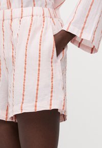 Linnebyxor med rosa och orange vertikala ränder, med elastiskt midjeband och fickor, mjuk textur och avslappnad design.