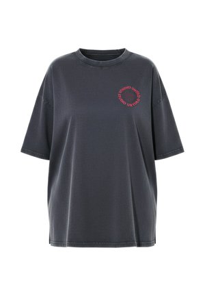 T-shirt oversize gris foncé à manches courtes et col rond, avec un texte circulaire rouge « STUDIO UNTOLD » sur la partie gauche de la poitrine.