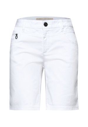 Zbliżenie osoby noszącej białe spodnie z przednią kieszenią na zamek błyskawiczny i metalowym pierścieniem przy suwaku, w połączeniu z czerwoną górą.