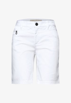 Nærbillede af en person iført hvide bukser med en lomme med lynlås foran og metalring på lynlåstrækket, kombineret med en rød top.