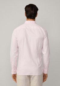 Light pink button-up shirt with long sleeves, classic collar, subtle texture, and button cuffs, viewed from the back against a neutral background.