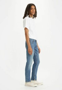  camiseta blanca de manga corta, jeans de mezclilla azul de corte ajustado y zapatillas deportivas blancas. Los jeans tienen un lavado desgastado y un corte recto.