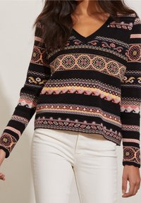 Sweter robiony na drutach, z dekoltem w kształcie litery V, czarna baza z wielokolorowymi wzorami geometrycznymi, długie rękawy oraz ściągacze u mankietów i na dole.