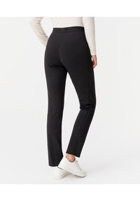 Zwarte getailleerde broek van rekbare stof, met een hoge tailleband en naaddetails, gecombineerd met witte sneakers.