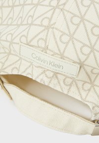 Calvin Klein pet met een roomkleurige achtergrond. Geometric patroon in lichtbeige. Heeft een textiele stof en een leren label met de merknaam.