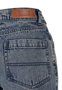 Denim jeans in a light blue wash, featuring a brown leather tag, stitched back pockets, and faded texture with a classic cut.
